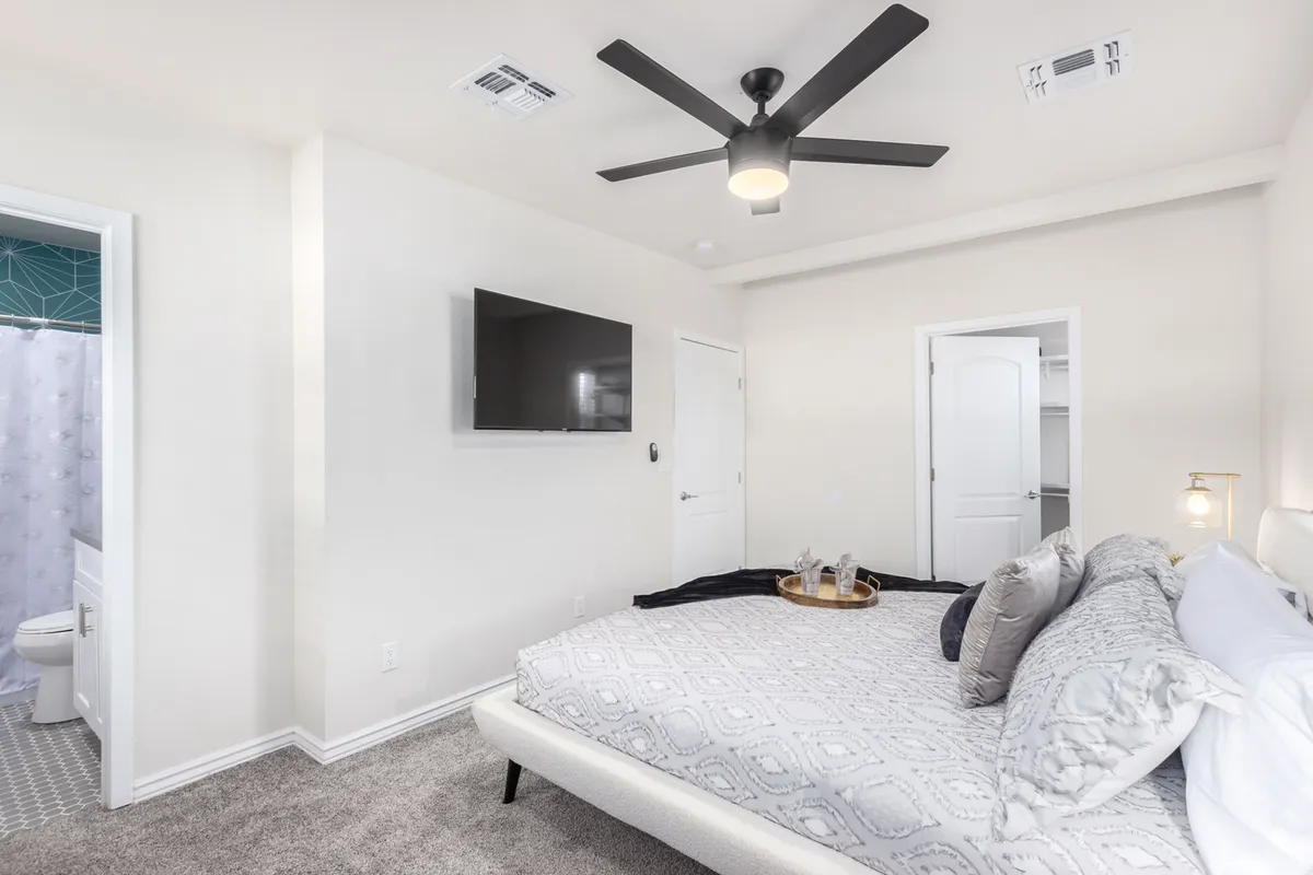 A cozy king bed adorned with decorative pillows is the focal point of this inviting master suite. A wall-mounted television, a sleek nightstand with a stylish tray, and soft lighting provide a relaxing and upscale atmosphere, ideal for unwinding after a long day. The room exudes a sense of comfort and privacy.