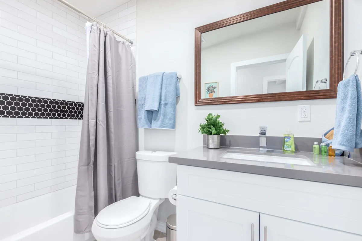 A bright and refreshing bathroom scene featuring a modern sink, mirror, and tiled shower area. The space is designed for comfort, offering a peaceful setting for morning routines or a relaxing bath after a lively night out.