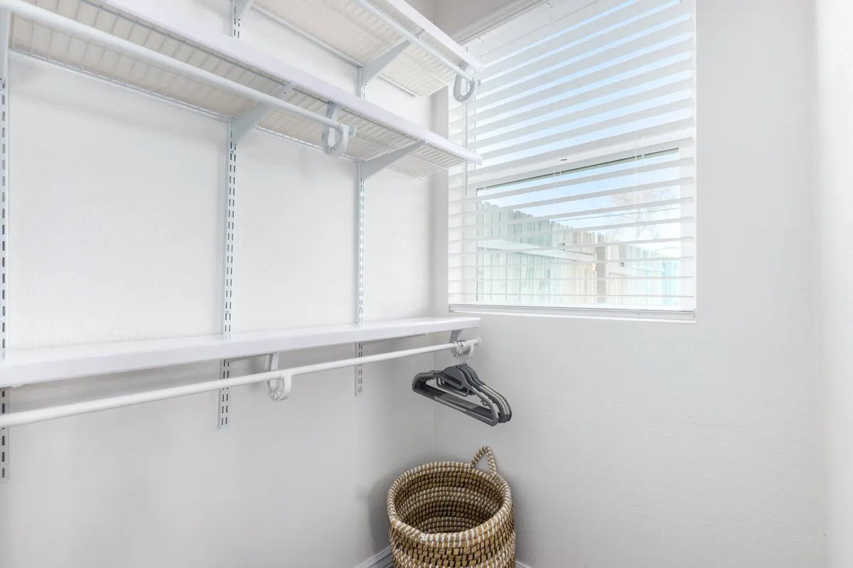 A calm, organized closet featuring shelves with neatly arranged items, hanging clothes, and a woven basket, suggesting both practical storage and thoughtful details that support a comfortable extended stay.