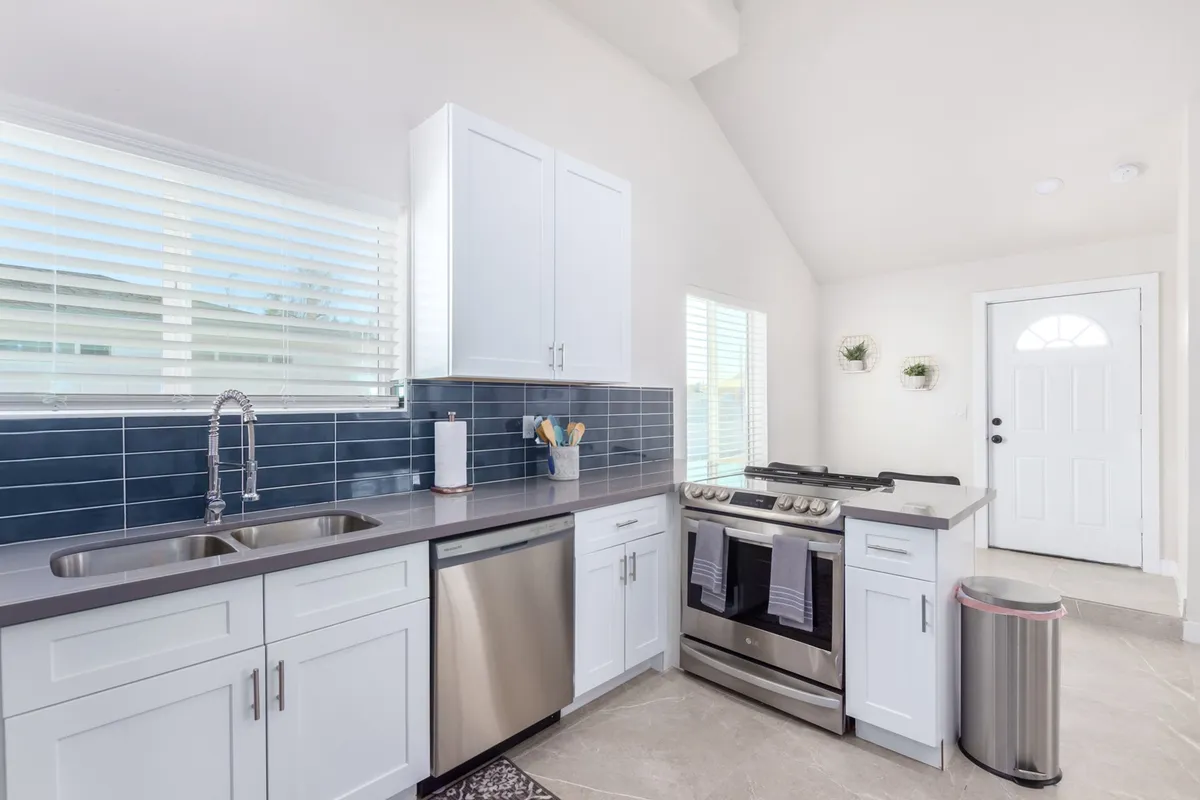 This photo highlights the kitchen’s stainless steel appliances, the eye-catching blue backsplash, and crisp white cabinetry. The arrangement is sleek and functional, emphasizing modern design and cleanliness.